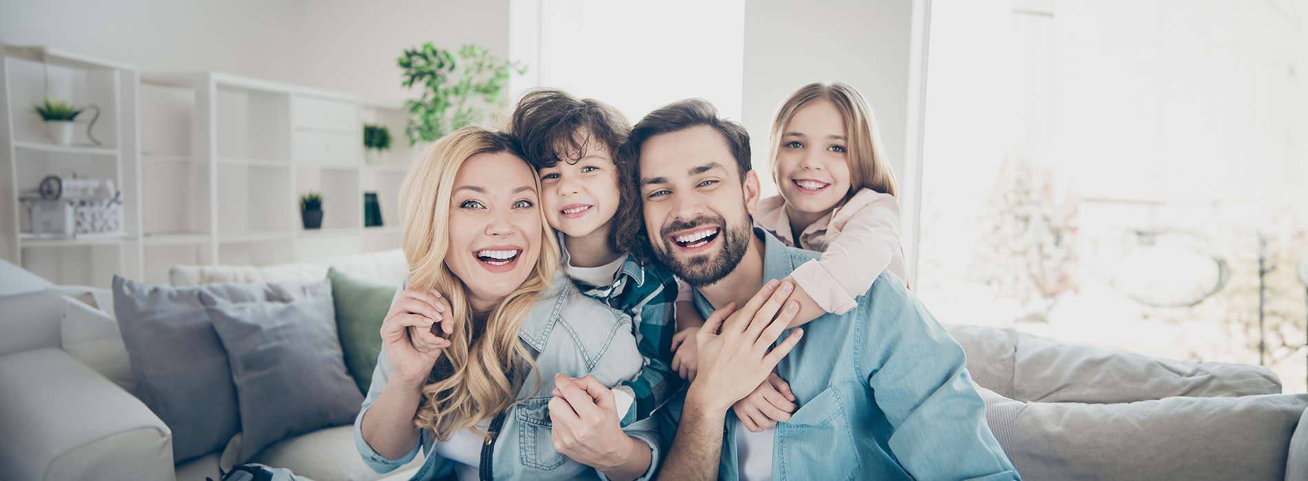 A family photo with four individuals, including adults and children, smiling and posing together in an indoor setting.