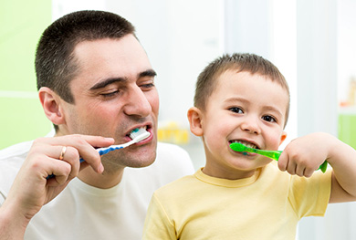 The image features a man and a young child brushing their teeth with toothbrushes.